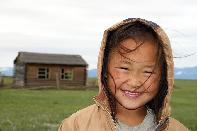 ילדה חייכנית וברקע בקתת העץ המשפחתית ליד רנצ'ינלומב, צפון מונגוליה 2010