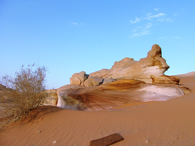 A colored sandstone rock erecting from the dunes of Wadi er Raqiya at sunset, 2006