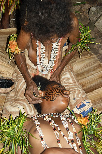 An artist demonstrates the process of tattooing a face of a young adolescent, Komoa Village 2009
