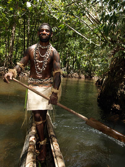 גבר מקומי בלבוש ואיפור מסורתיים חותר בקאנו מעץ, הכפר קומואה 2009