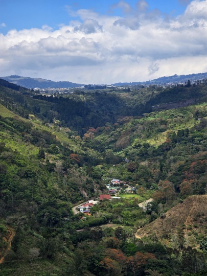 A small cluster of houses with colorful roofs in the lower part of a lush, green mountain valley, 2026