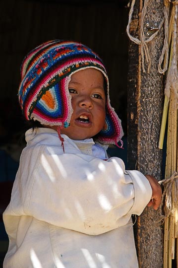 A cute little Aymara boy with a warm and colorful knitted hat, at the entrance of his Totora reeds hut, Islands of Uros, Lake Titicaca 2008