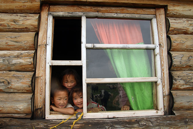 Smiling children in a window of a family wooden hut near Renchinlkhumbe, North Mongolia 2010