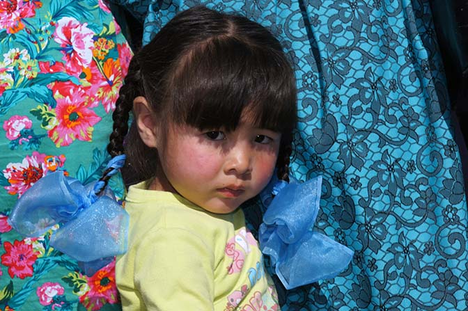 Girl clings to her mother's dress in Tashanta village, 2014