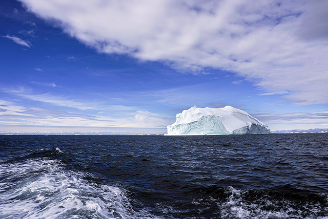 Floating iceberg, and in the water a trail of foam from the boat, 2017